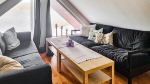 Un salon chaleureux avec un canapé noir, une table basse en bois et une vue sur un immeuble en briques rouges, visible à travers une grande fenêtre.
