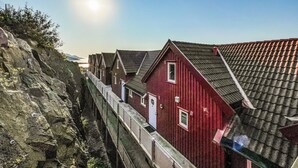 Une rangée de bâtiments en bois peints en rouge, avec un mur de soutènement en pierre et une passerelle métallique.
