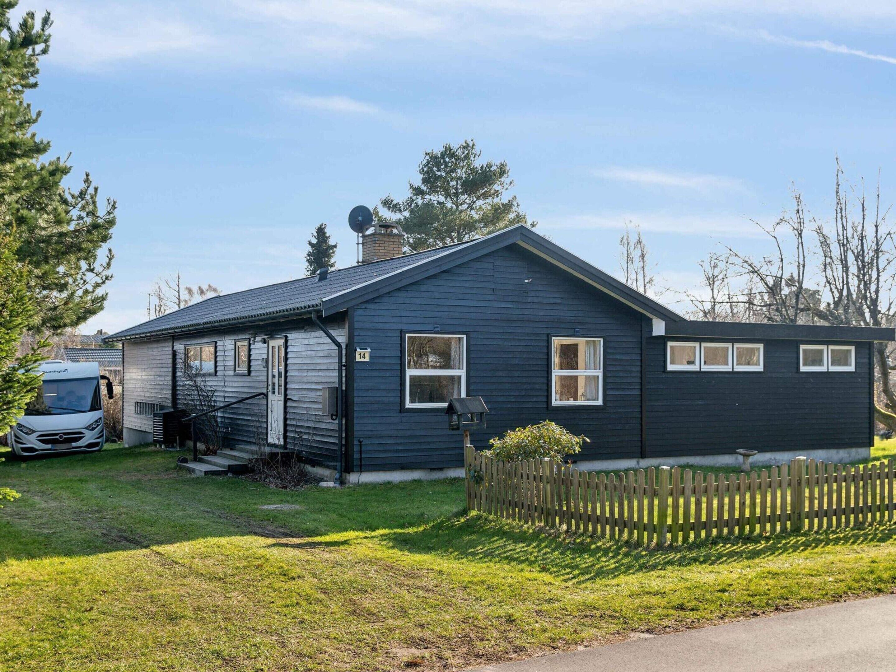 Et etplanshus med mørkeblå facade, en parabolantenne på taget og en lille indhegnet have.