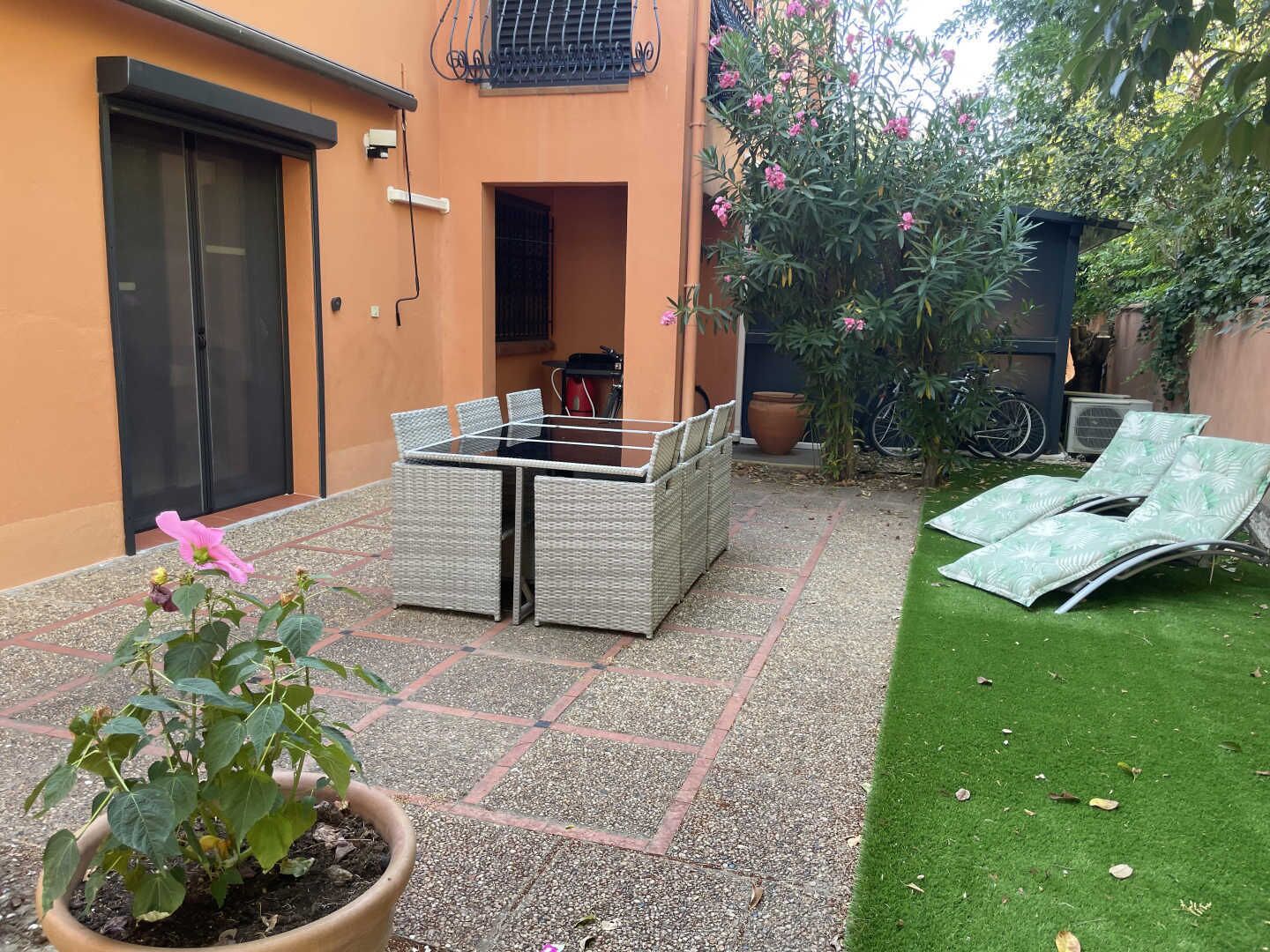 A patio with a table and chairs, a potted plant, and a lawn.