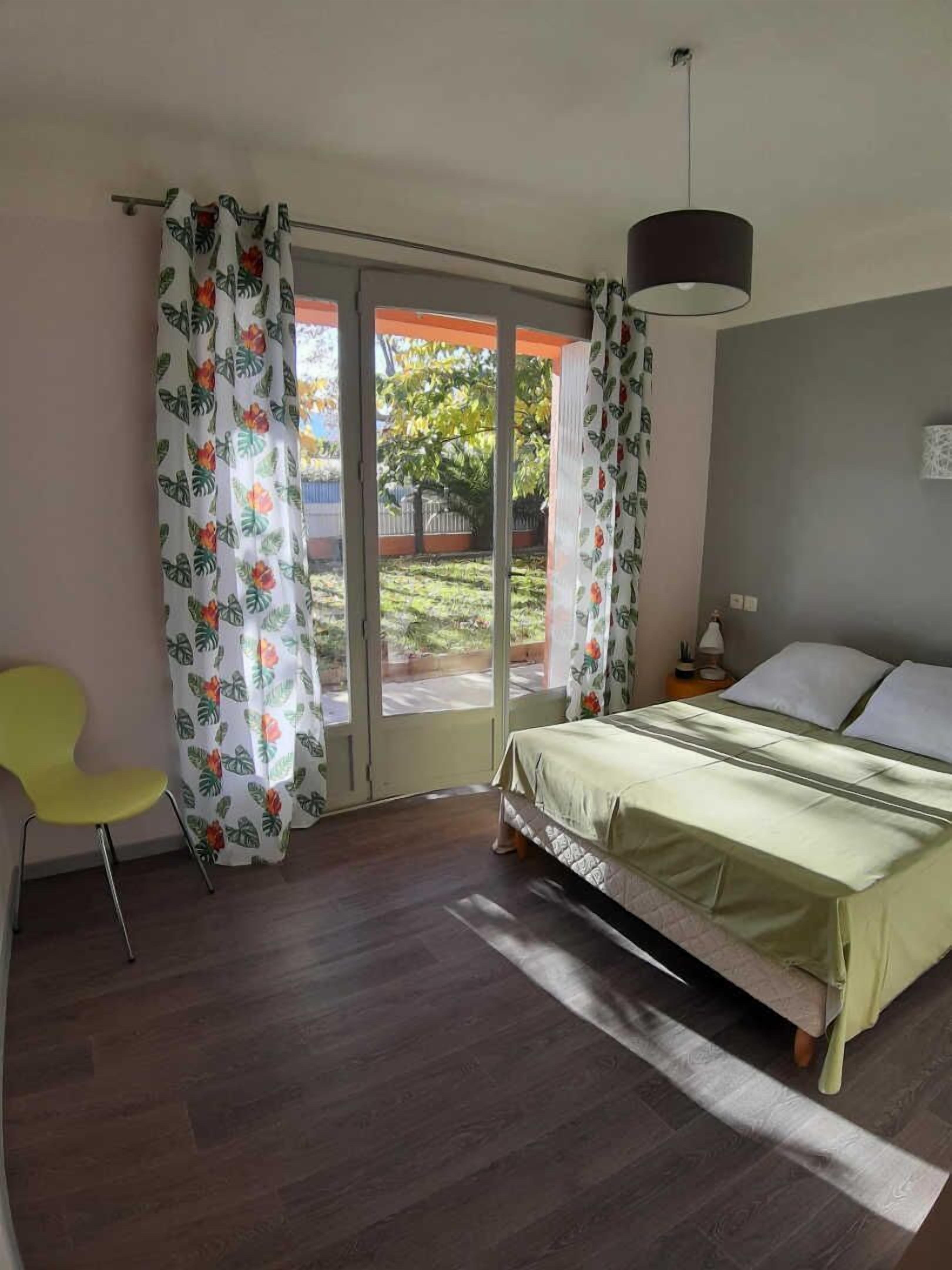 A bedroom with a bed, a chair, and a view of the outdoors through a glass door.