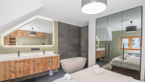 A modern bathroom with a freestanding bathtub, a large mirror, and wooden cabinetry. - Duplex Veyra - Welkeys (Megève)