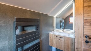 A modern bathroom with a large mirror, wooden cabinets, and a sleek black towel rack. - Duplex Veyra - Welkeys (Megève)