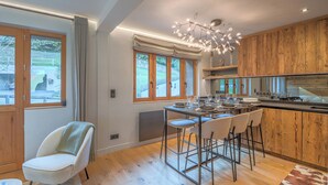 A modern kitchen with a central island, wooden cabinets, and a dining area with bar stools. - Duplex Veyra - Welkeys (Megève)