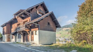 A wooden chalet with a balcony, a sloped roof, and a view of a village in the background. - Duplex Veyra - Welkeys (Megève)