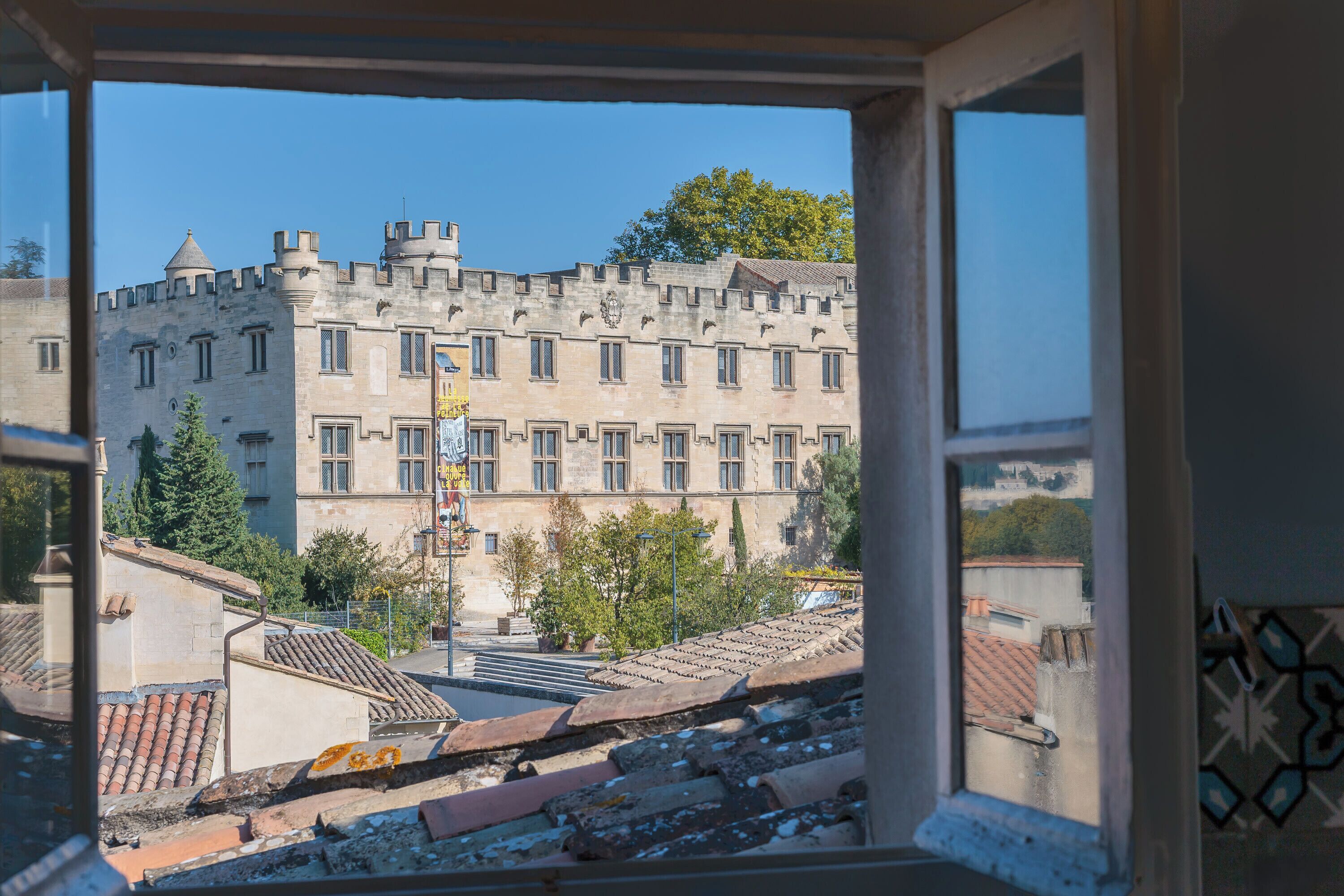 A view from a window of a building with a castle-like facade, a tiled roof, and a clear sky.