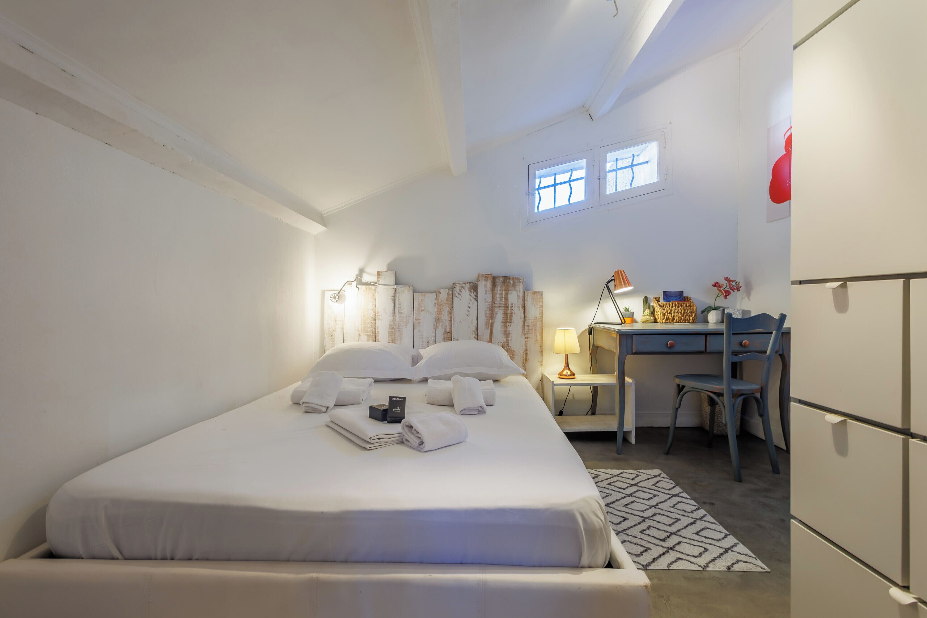 A neatly arranged hotel room with a bed, a desk, a chair, and a small table.