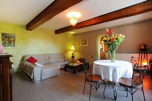 Een gezellige woonkamer met een bank, een eettafel met stoelen, een lamp en een bloemenvaas.