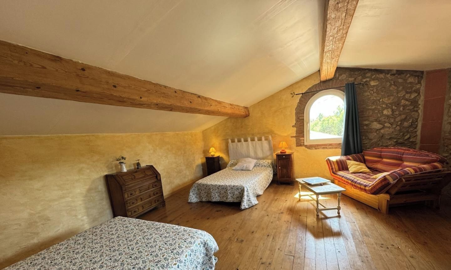 Una camera da letto mansardata accogliente con due letti, una cassettiera in legno, un tavolino e un divano.