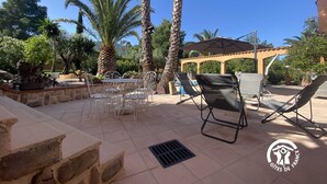 Un patio al aire libre con mesa y sillas, palmeras y una pérgola.