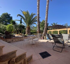 Une terrasse extérieure avec une table et des chaises, des palmiers et une pergola.