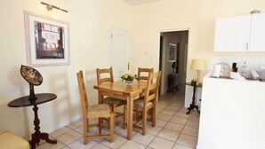 A dining area with a wooden table and chairs, a small round table with a decorative item, and a kitchen area with cabinets and a refrigerator. - Boucheron - ST-LAURENT-DE-CERDANS (ST-LAURENT-DE-CERDANS)