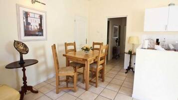 Un coin repas avec une table et des chaises en bois, une petite table ronde agrémentée d’un objet décoratif, et un espace cuisine avec des placards et un réfrigérateur.
