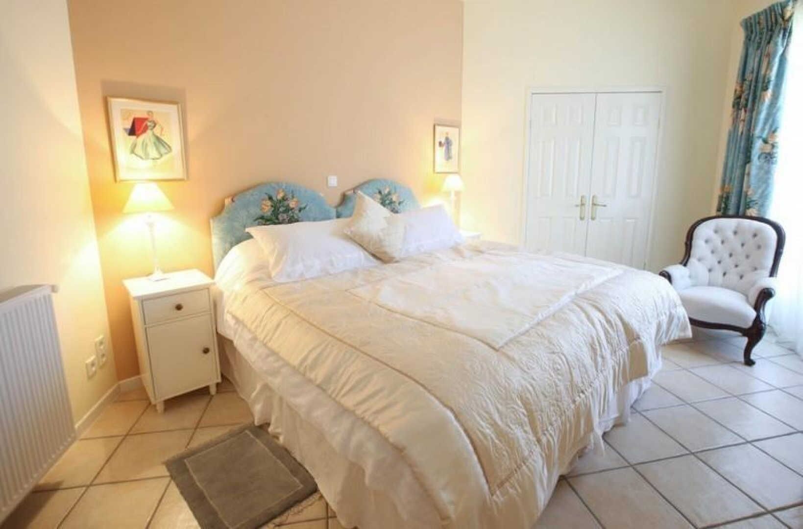 Une chambre à coucher avec un grand lit, une table de chevet, une chaise et une porte.