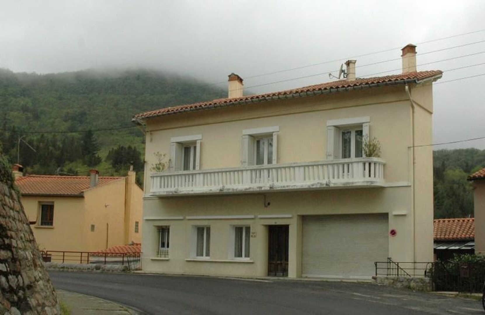 Un bâtiment à deux étages doté d’un balcon à l’étage supérieur, d’une porte de garage et ayant une chaîne de montagnes en arrière-plan.