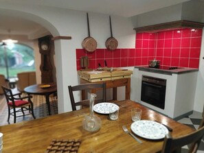 Uma cozinha com azulejos vermelhos, uma mesa de madeira com pratos, um vaso e um relógio.