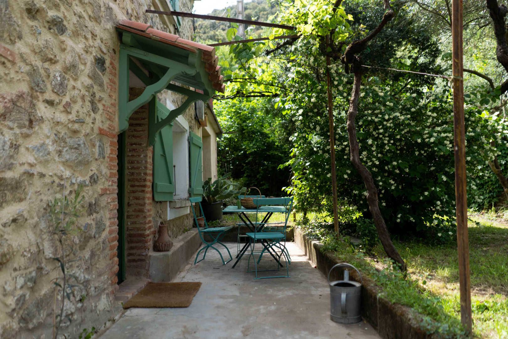 A stone building with a small outdoor seating area, including a table and chairs, and a potted plant.