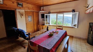 Un intérieur en bois comprenant une table à manger, des chaises, un banc, une fenêtre donnant sur un paysage agréable et un ventilateur de plafond.