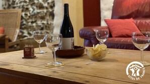 A wooden table with a wine bottle, glasses, a bowl of snacks, and a sign for 'BAR TAPAS'. A red leather couch and a stone wall are in the background.