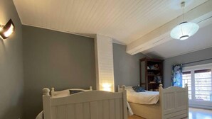 A bedroom with two beds, a window with blinds, a radiator, and a ceiling light fixture.