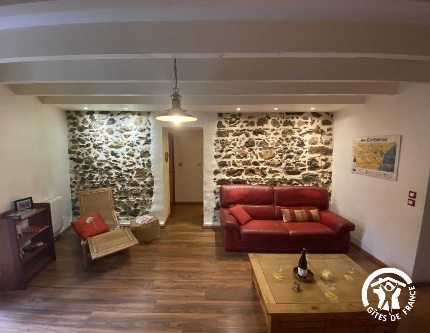 A cozy living room with a red leather sofa, a wooden coffee table with wine glasses, a stone wall, and a hanging light fixture.