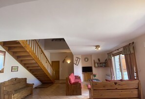 Un espacio habitable amplio con una escalera de madera, un televisor y una zona de estar acogedora.
