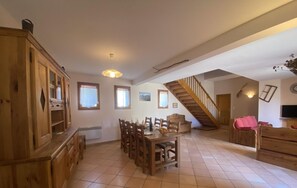 Amplia sala de estar con mesa de comedor, armarios de madera, una escalera y un televisor.