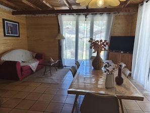 Un intérieur en bois comprenant une table à manger, des chaises, un canapé, un téléviseur et une fenêtre avec des rideaux.