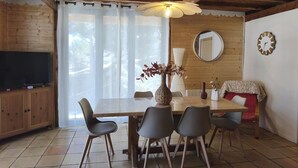 A wooden dining area with a table, chairs, a TV, and a window with curtains. - Formi-Dable - FORMIGUERES (FORMIGUERES)