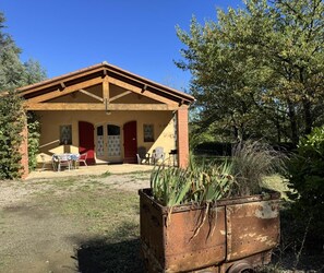 Um edifício rústico com um alpendre, uma porta vermelha e uma pequena mesa com cadeiras.