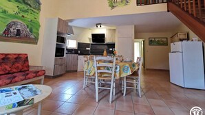 Een gezellige woonkamer met een rode bank, een eettafel gedekt voor vier personen, en een keuken op de achtergrond.