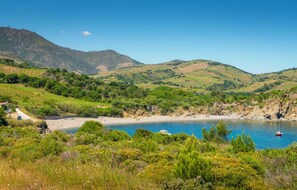 A coastal landscape with a beach, boats, and mountains in the background.