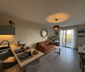 A modern living room with a sofa, a dining table with plates and glasses, and a TV.