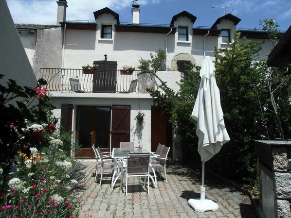 A courtyard with a patio table and chairs, a white umbrella, and a building with a balcony and windows.