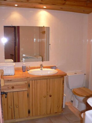 A bathroom with a wooden vanity, a sink, a mirror, and a toilet.