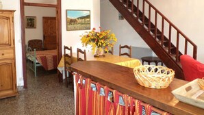 A dining area with a wooden table, chairs, a vase of flowers, a wicker basket, and a staircase. - Mas Terrats - PONTEILLA (PONTEILLA)