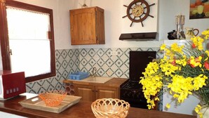 A kitchen with a wooden cabinet, a ship's wheel clock, a stove, and a vase of yellow flowers. - Mas Terrats - PONTEILLA (PONTEILLA)