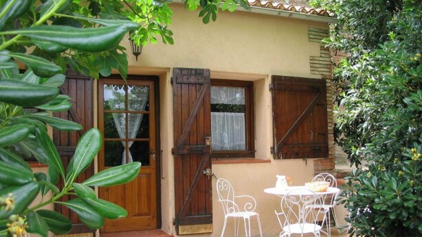 A house with a patio area featuring a table and chairs, a wooden door, and a window with shutters. - Mas Terrats - PONTEILLA (PONTEILLA)