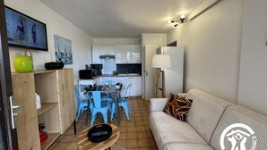 A compact living space with a kitchenette, a dining area with blue chairs, a sofa with patterned cushions, and a small table with a tray. - Gîte de la Lagune - SAINT CYPRIEN (SAINT CYPRIEN)