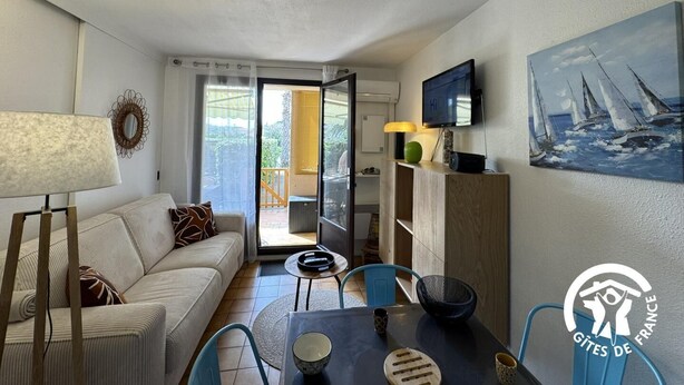 A compact living space with a sofa, a dining table, a TV, and a painting. - Gîte de la Lagune - SAINT CYPRIEN (SAINT CYPRIEN)