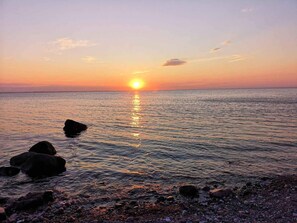 A sunset over a calm sea with rocks in the foreground. - 5 Star Holiday Home in Martofte (Martofte)