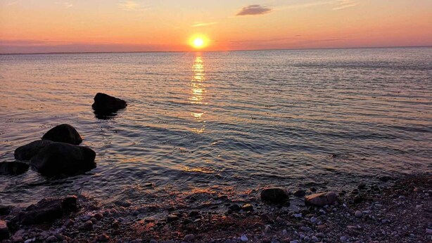 A sunset over a calm sea with rocks in the foreground. - 5 Star Holiday Home in Martofte (Martofte)