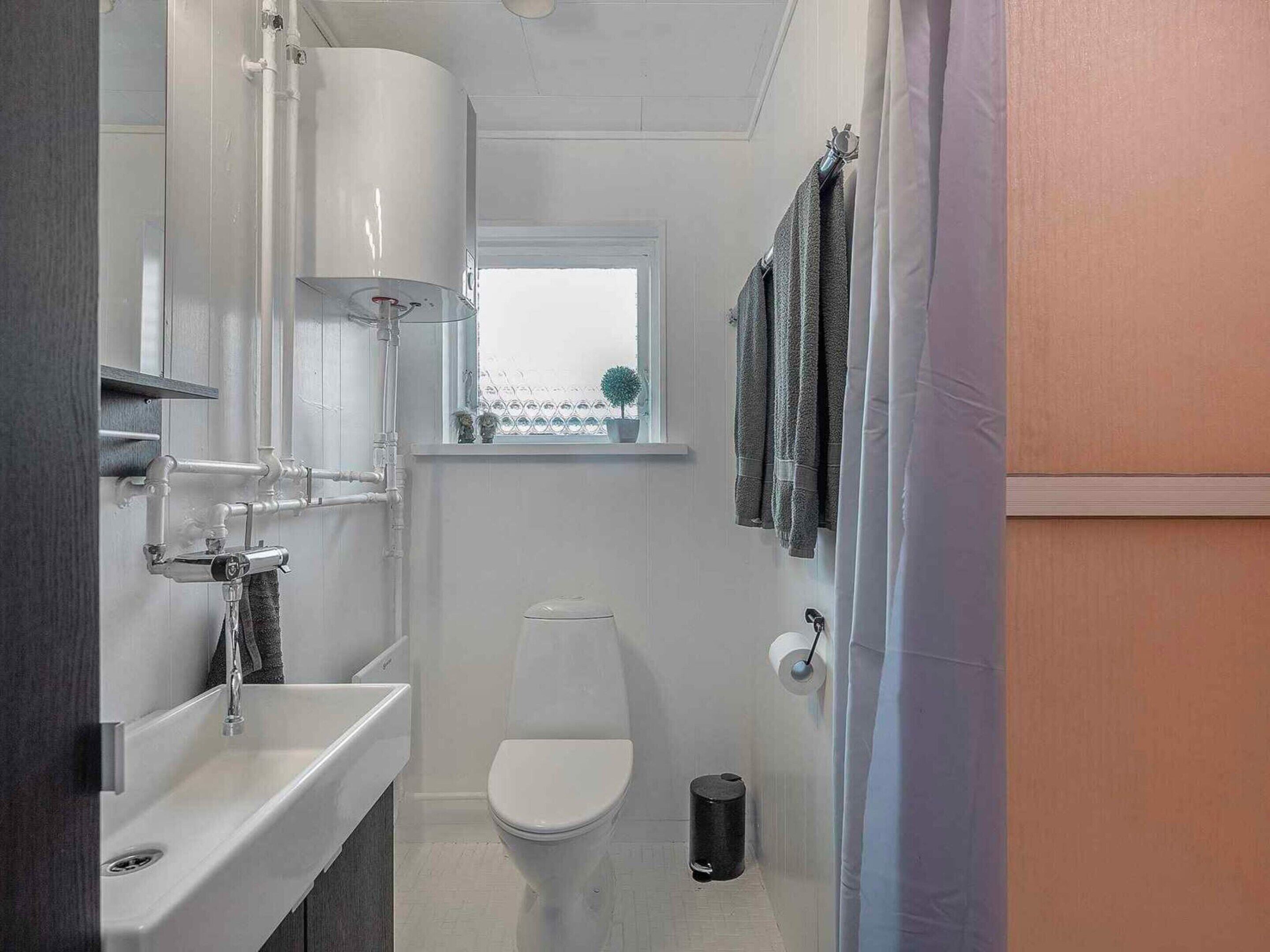 Et lille badeværelse med en hvid vask, toilet og et vindue over toilettet.