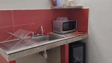 Una cucina compatta con lavandino, forno a microonde e piccolo frigorifero.