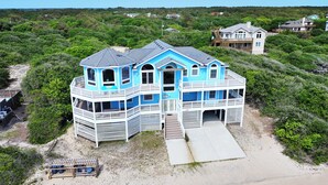 Una casa frente al mar de dos pisos, con balcón, porche cubierto y camino de entrada de arena.
