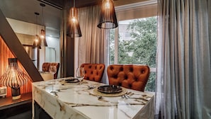Uma sala de jantar com mesa de mármore, cadeiras de couro, luminárias pendentes e vista através de grandes janelas.