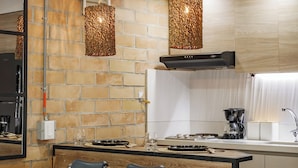 Cozinha moderna com parede de tijolos, bancada de madeira, duas luminárias pendentes e uma pia embutida.