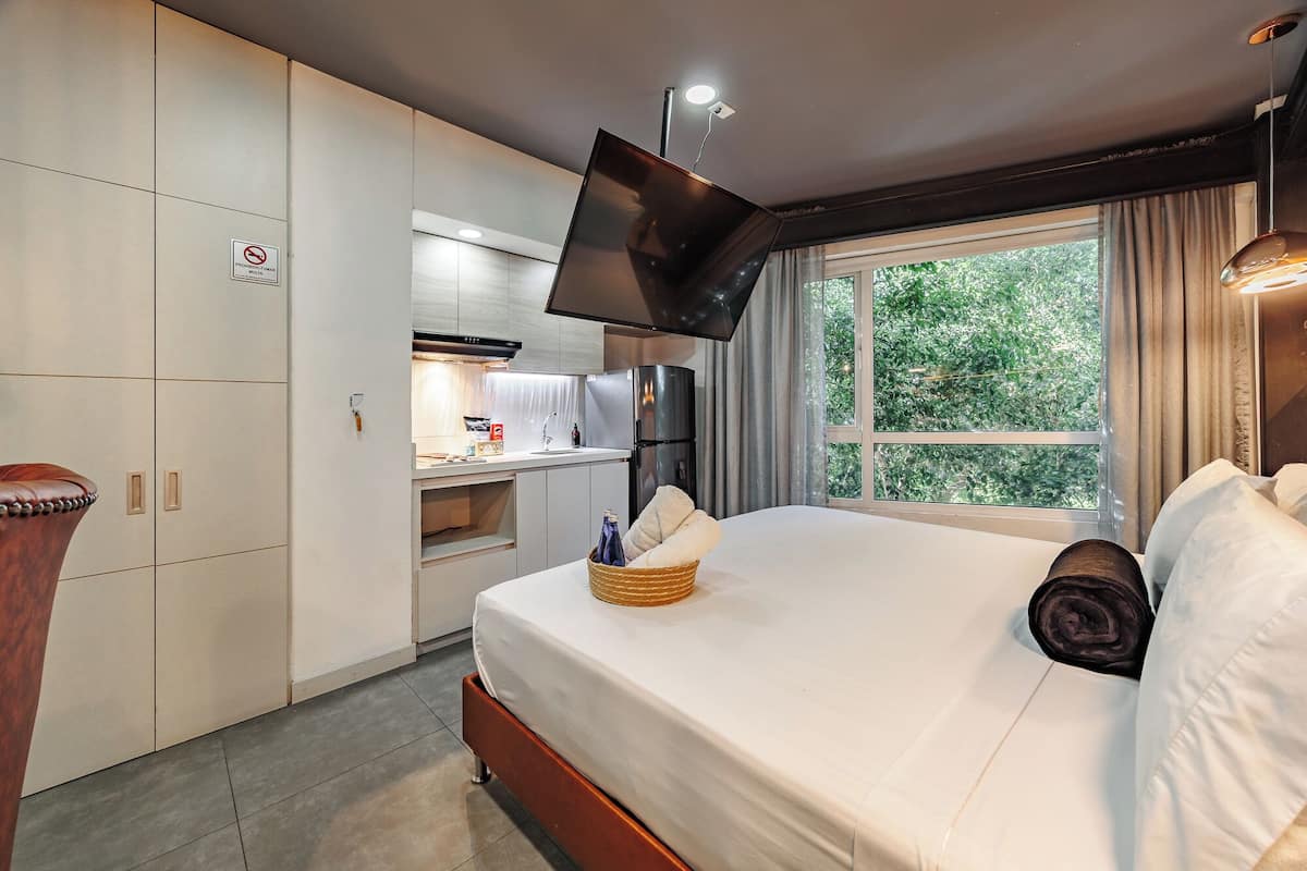 A hotel room with a bed, a desk, a television, and a window with a view of trees.