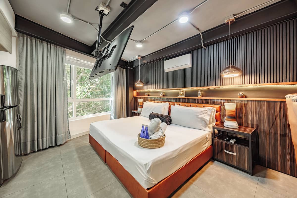 A modern hotel room with a large bed, a bedside table, a built-in TV, and a window with curtains.