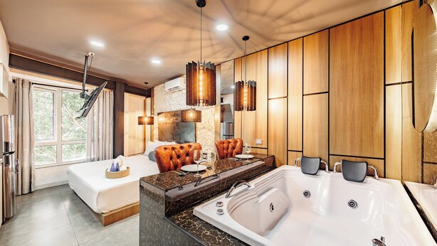 Quarto de hotel moderno com uma cama grande, área de estar com sofá e mesa, banheiro separado com banheira e vista para o verde lá fora.